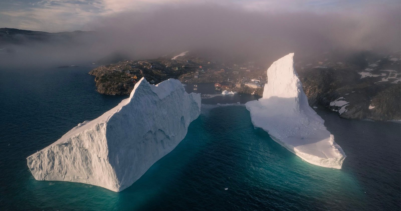 Surreal Photos of Gigantic Icebergs Looming Over a Tiny Village Surreal Photos of Gigantic Icebergs Looming Over a Tiny Village
